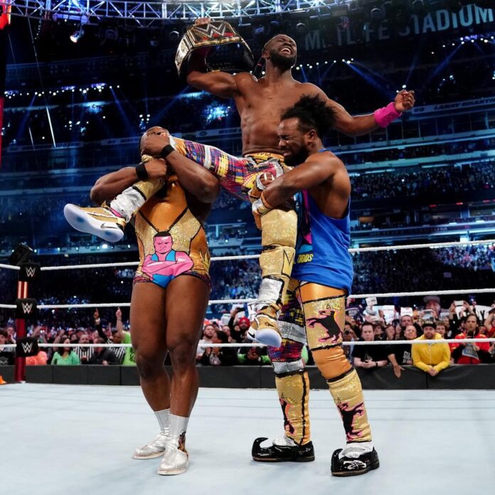 New Day members Xavier Woods and Big E holding up WWE Champion Kofi Kingston at WrestleMania 35